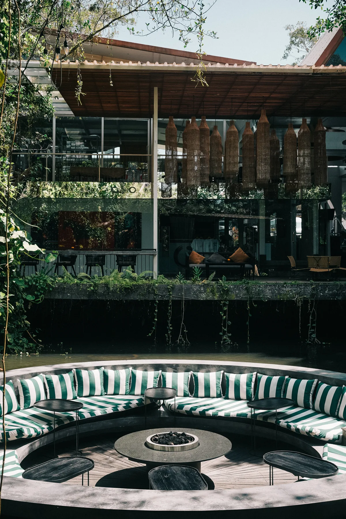 A modern timber building with a sweeping roof above a round outdoor seating landscape with a central fire pit