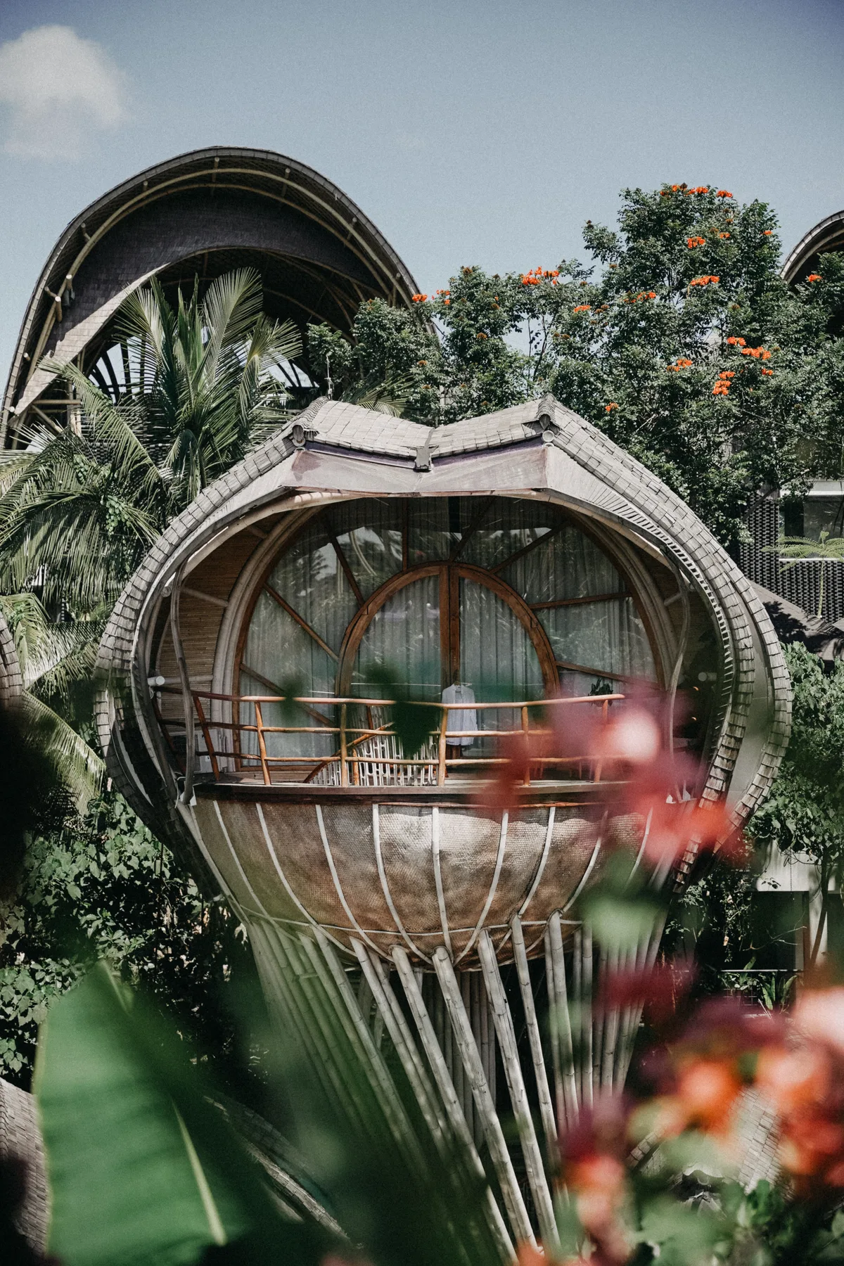 An egg-shaped bamboo treehouse suite elevated on stilts among jungle trees and orange blossoms at Nuanu