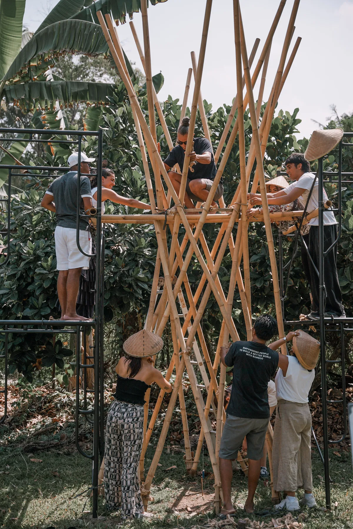 Students on scaffolding lashing bamboo poles together at the top of a tall conical structure at BambooU