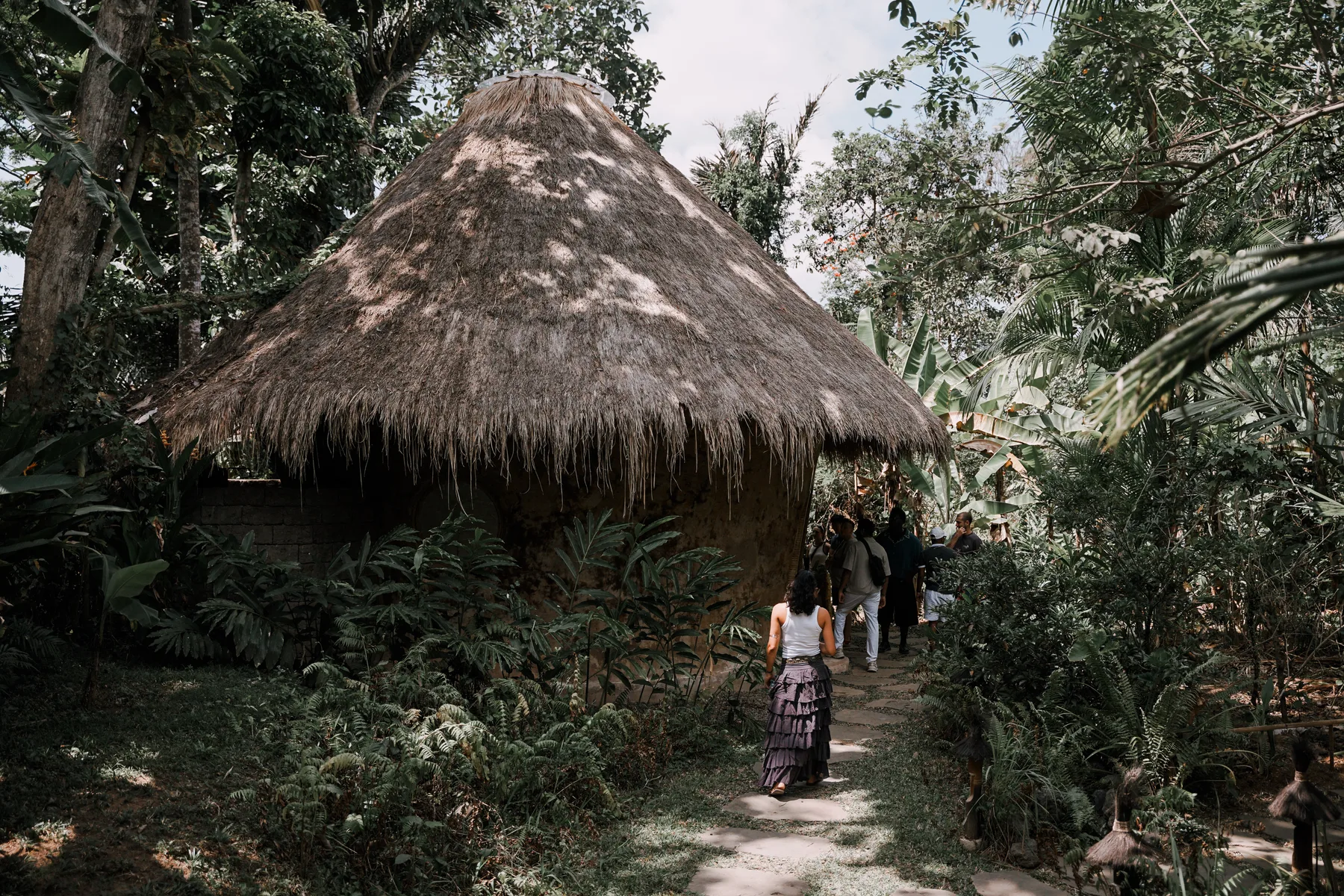 A round, reed-thatched bamboo hut deep in the jungle at BambooU, the group walking toward it on a stone path