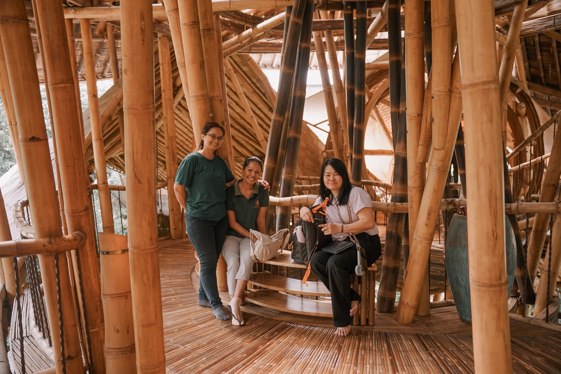 Students on a spiral staircase inside a bamboo house at Green Village, surrounded by the bundled bamboo columns that carry the roof