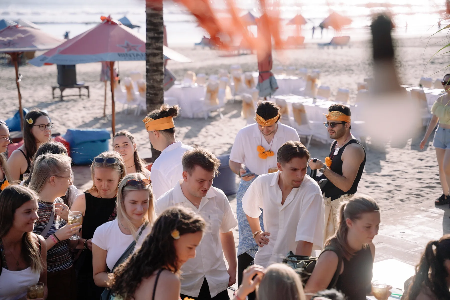 Students mingling on the beach at sunset before the welcome dinner, dinner tables set up behind them