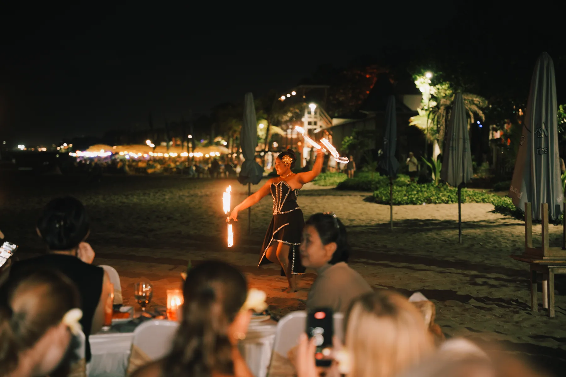 A fire dancer performing on the beach at night, students watching from their dinner tables