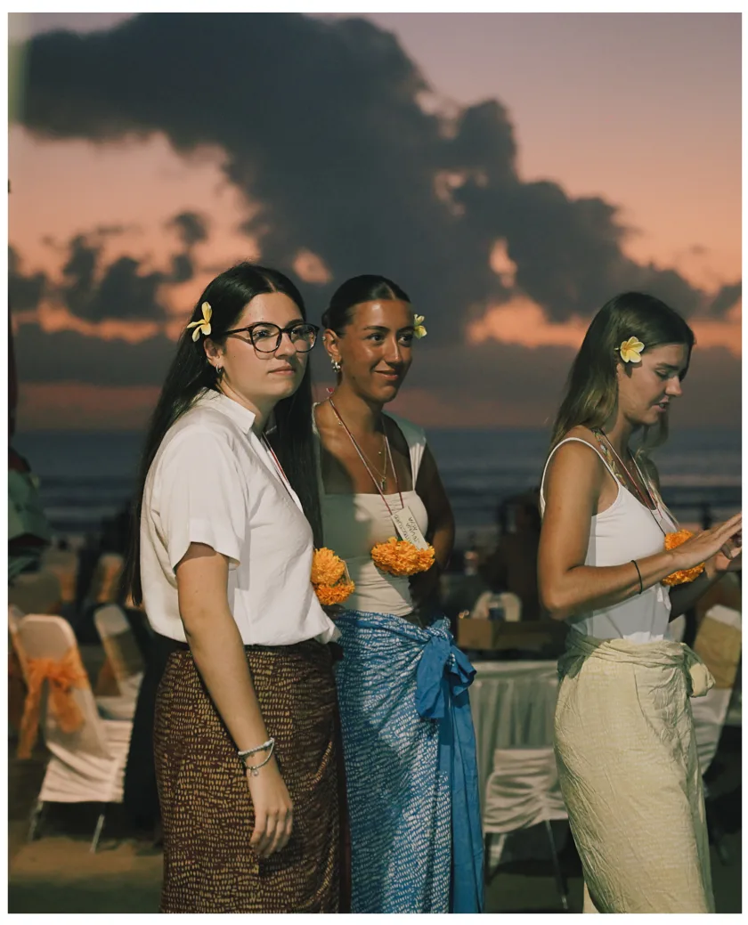 Three students standing together on the beach at sunset, flowers in their hair